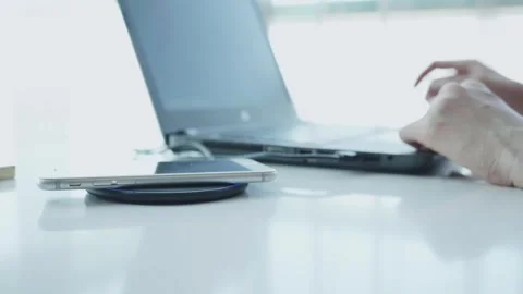 A laptop is open on a wooden table with a small silver device on the table Stock Footage 313597573