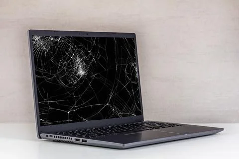 Laptop pc with a broken screen in cracks on a gray background close up Stock Photos