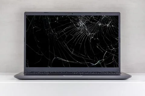 Laptop pc with a broken screen in cracks on a gray background close up front  Stock Photos