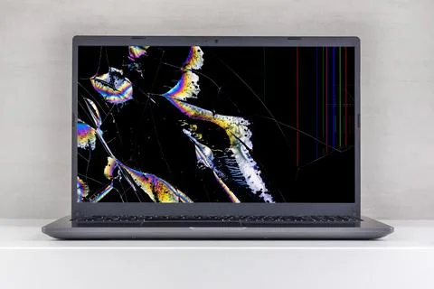 Laptop pc with a broken screen in cracks on a gray background close up front  Stock Photos