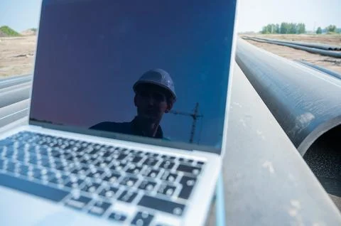 Laptop on pipes at a construction site. Reflection of a portrait of a builder in Stock Photos