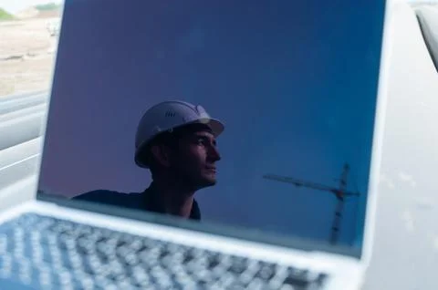Laptop on pipes at a construction site. Reflection of a portrait of a builder in Stock Photos