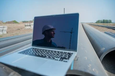 Laptop on pipes at a construction site. Reflection of a portrait of a builder in Stock Photos