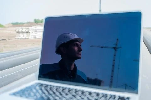 Laptop on pipes at a construction site. Reflection of a portrait of a builder in Stock Photos