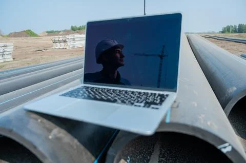 Laptop on pipes at a construction site. Reflection of a portrait of a builder in Stock Photos