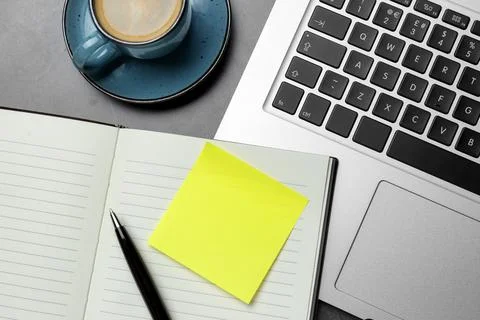 Laptop, planner, empty sticky note, pen and cup of coffee on grey table, flat Stock Photos