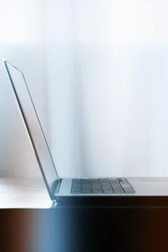 Laptop sits on a table with soft light coming through a window in a quiet room Stock Photos