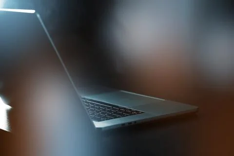 Laptop sits on a table with soft light reflecting on it during an indoor setting Stock Photos