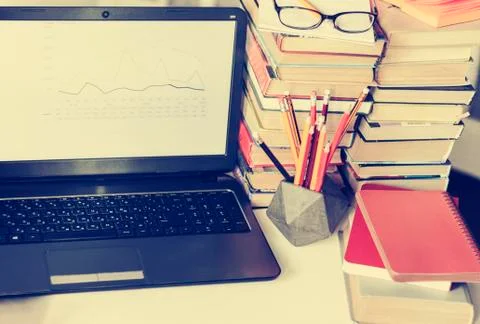 Laptop, stack of books, notebooks and pencils on white table, education offic Stock Photos