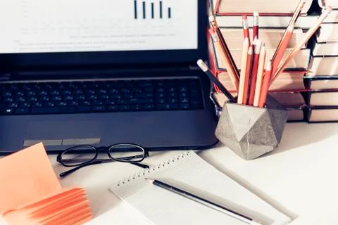 Laptop, stack of books, notebooks and pencils on white table, education offic Stock Photos