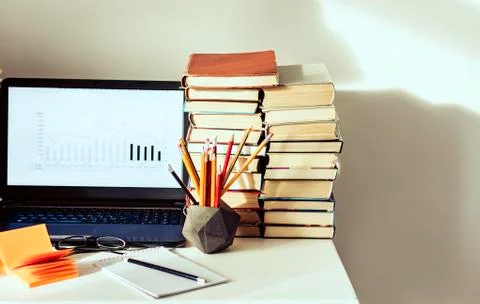 Laptop, stack of books, notebooks and pencils on white table, education offic Stock Photos