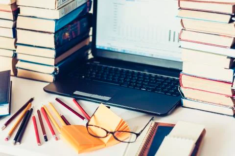Laptop, stack of books, notebooks and pencils on white table, education offic Stock Photos