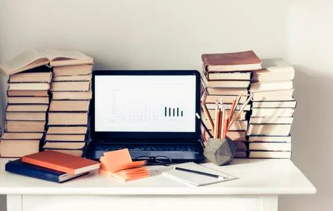 Laptop, stack of books, notebooks and pencils on white table, education offic Stock Photos