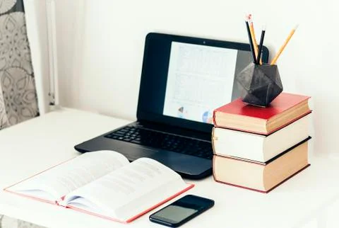 Laptop, stack of books, smartphone, notebook and pencils in concrete holder o Stock Photos