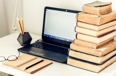 Laptop, stack of old books, notebook and pencils on white table, education re Stock Photos