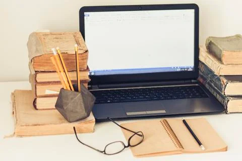 Laptop, stack of old books, notebook and pencils on white table, education re Stock Photos