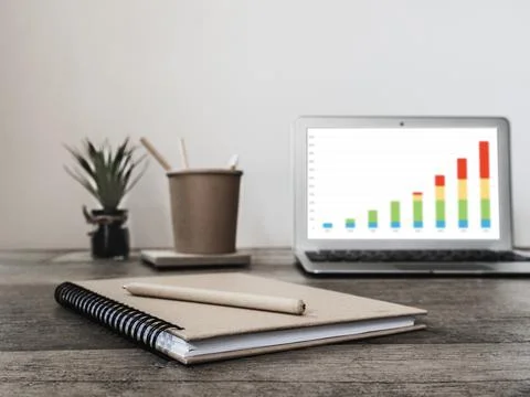 Laptop with statistics chart on screen, flower and office supplies. Horizontal Stock Photos
