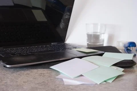 Laptop surrounded by scattered sticky notes, a water glass, and office tools Stock Photos