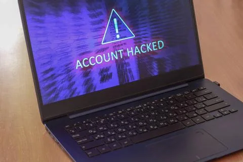 Laptop on the table and on a blue screen the text account is hacked. Warni... Stock Photos