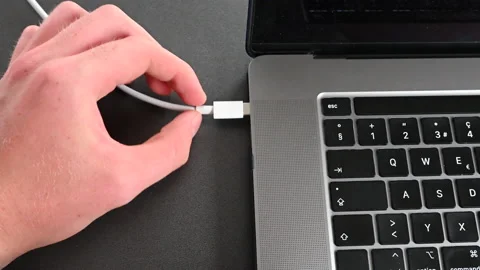A laptop user plugs in a cable to charge his computer's battery Stock Footage 212246069