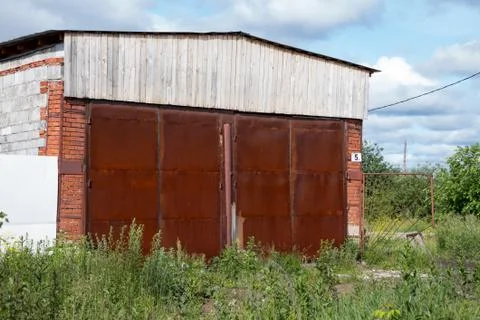 Large abandoned hangar with a rusty gate and overgrown grass entry Foto stock
