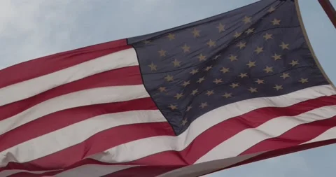 Large American Flag against blue sky blowing in the wind slow motion Stock Footage 166326858
