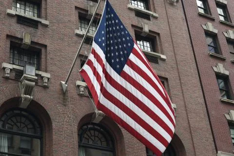 A large American flag flying from the side of a brick building Stock Photos