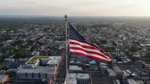 Large American flag waves atop tall flagpole above downtown Allentown Stock Footage 340969416