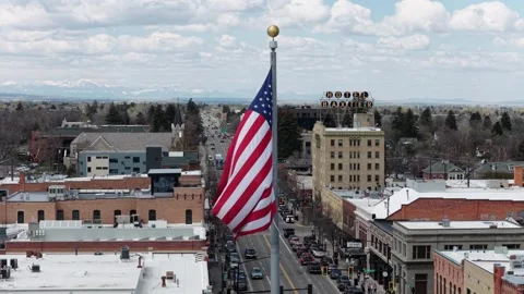 Large American flag waves over downtown Bozeman main street with traffic Stock Footage 337452306