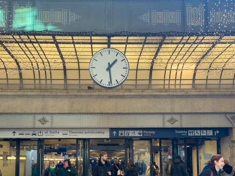 A large analog station clock hangs above the bustling entrance hall of an old Photos
