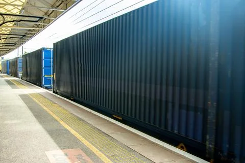 A Large And Powerful Freight Train Passing By A Station Platform Pulling It.. Stock Photos