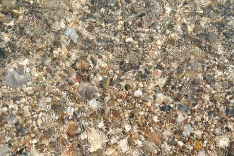 Large and small multi-colored pebble stones on the beach under clear water Stock Photos