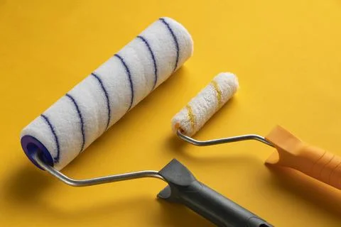 Large and small paint roller on yellow background. Stock Photos
