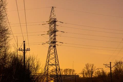 Large angular anchor support of power lines behind trees against the sunset s Stock Photos