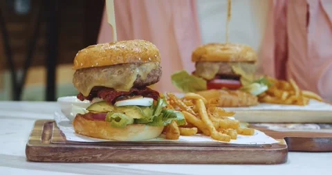 Large appetizing burger with meat and vegetables stands on the table next to a Stock Footage 249997190
