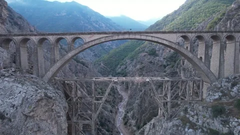 Large arched viaduct bridge crosses mountain valley with rocky sides under Stock Footage 342704090