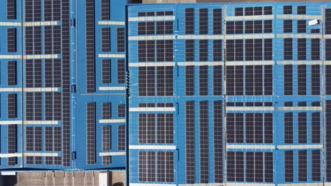Large array of solar panels mounted on blue industrial rooftops viewed from Stock Footage 345103303