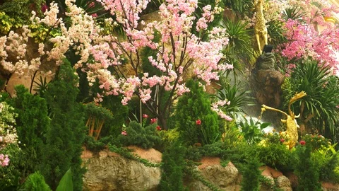 A large artificial waterfall framed by pink flowers and green leaves. Stock Footage 100191504