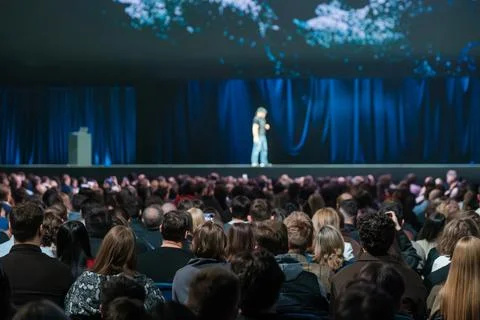 Large audience watching speaker on stage at technology conference with blue Stock Photos