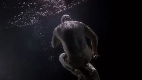 A large bald man without a shirt hovers in the dark under the water in the pose Vídeos de archivo 166165541