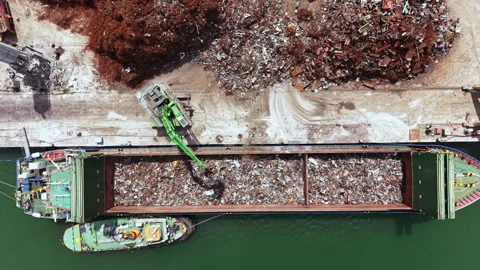 Large barge loaded with scrap metal docks at a port while machinery works to Stock Footage 337911786