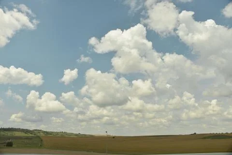 A large beautiful white cloud hangs low over a green field during the day Stock Photos