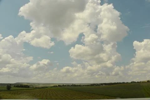 A large beautiful white cloud hangs low over a green field during the day Stock Photos