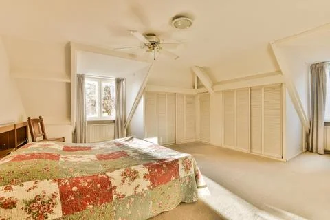 A large bedroom with a bed and a ceiling fan Stock Photos