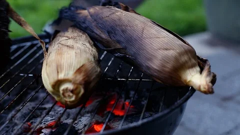 A large beef brisket and corn in the husk being barbequed on a small charcoal Stock Footage 111446789