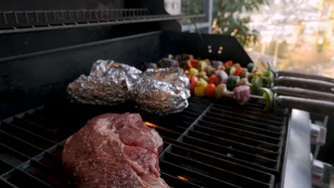 Large beef steak grilling on a bbq with a man turning vegetable kebabs Video stock 86002367