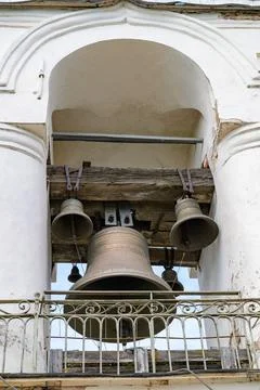 Large bell hangs within an arched stone bell tower. Smaller bells rest above, Stock Photos