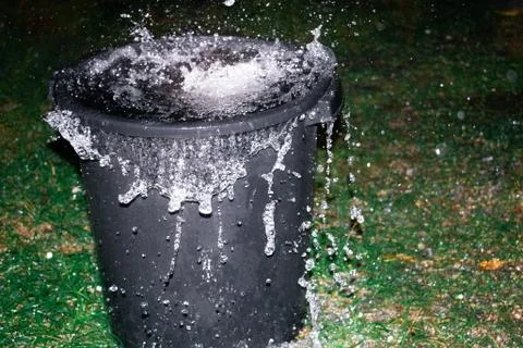 A large black bin overflows with rain water from a tropical storm Photos