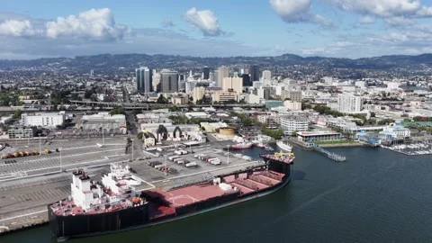 Large black bulk cargo ship docks at Oakland's busy industrial waterfront Stock Footage 340042507