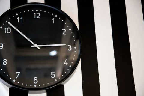 Large black clock on the striped wall of the room Stock Photos